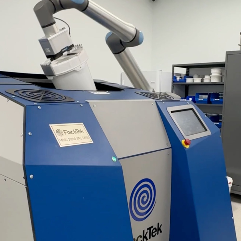 A collaborative robot arm loading a FlackTek mixer